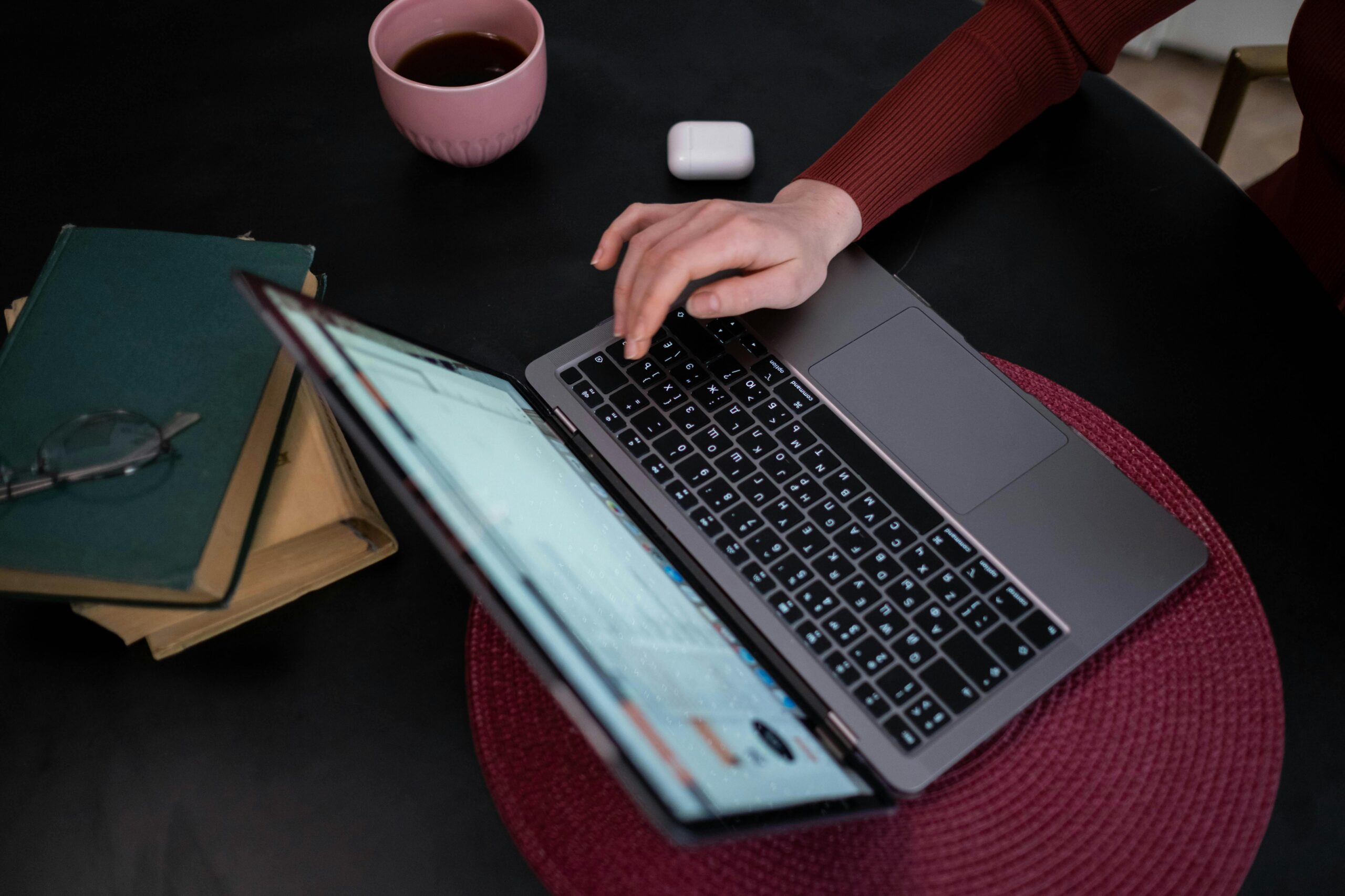 A person typing on a laptop with coffee and books nearby, creating a cozy work environment.